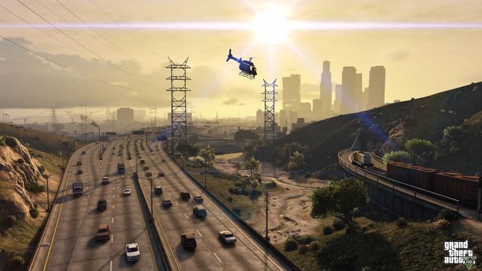 A helicopter flying low over a freeway. A train is heading into a tunnel, skyscrapers can be seen in the background, with the sun starting to set.