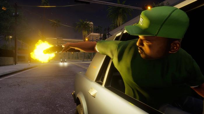 A man in a green tee shirt and baseball gap hangs out the back window of a car and fires a gun at a chasing vehicle.