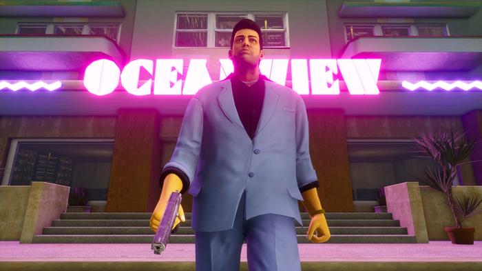 A man in a blue suit and black shirt walks away from a building with a magnum gun in his hand. the building has pink neon letters spelling out Ocean View.