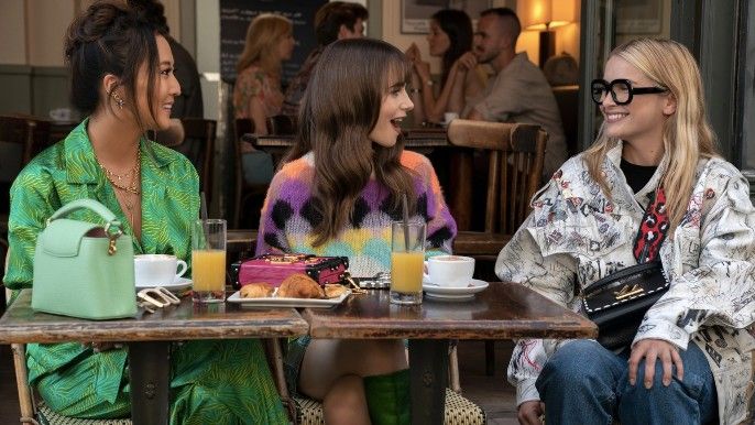 Ashley Park as Mindy, Lily Collins as Emily, Camille Razat as Camille sit in a cafe in Emily in Paris Season 3