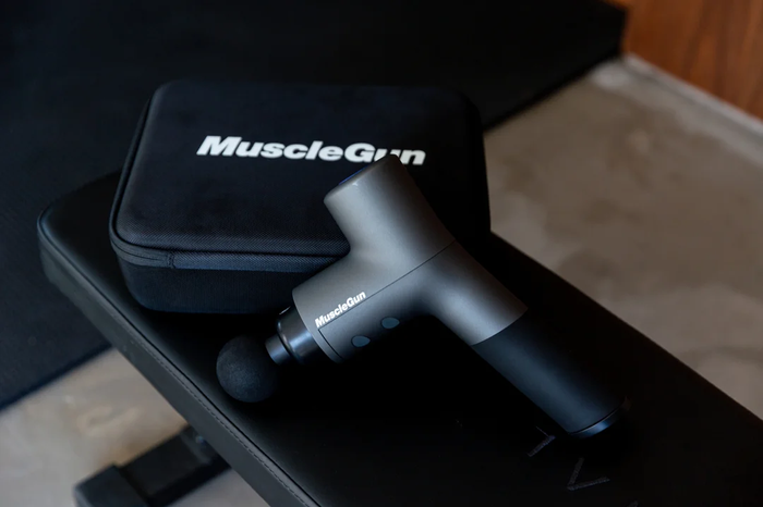 Musclegun Carbon with carry case on a gym bench