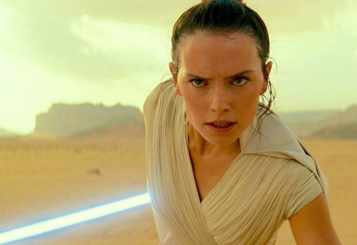 Rey holds a blue lightsaber in a desert.