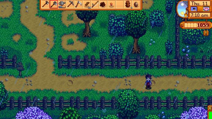 Stardew Valley. A rainy day in Pelican Town in Spring Year 1. The player is standing on a dirt path in the rain. The clock is visible in the top right of the screen. The clock is showing that it is morning on Thursday 11 in Spring. The tools/inventory menu is at the top of the screen and it is full. 