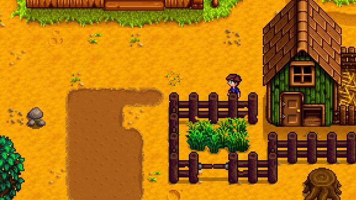 Stardew Valley. The player is stood beside their basic coop and behind their wooden fence. The wooden fence encloses the outside of the coop and has a small section of grass to the left of the coop for the chickens. 