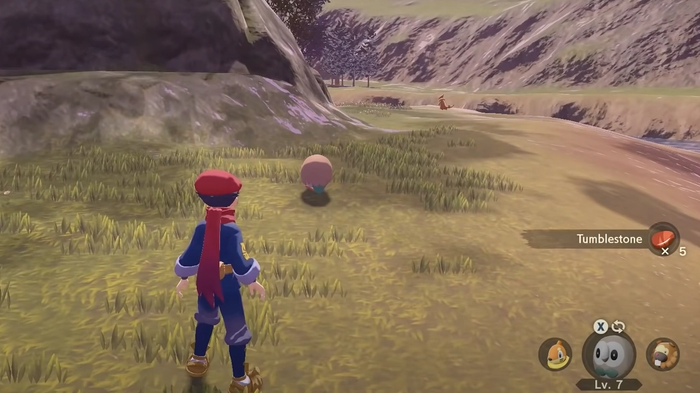 A Pokémon Trainer uses their Rowlet to farm Tumblestone from a rock in Obsidian Fieldlands of Pokémon Legends: Arceus.