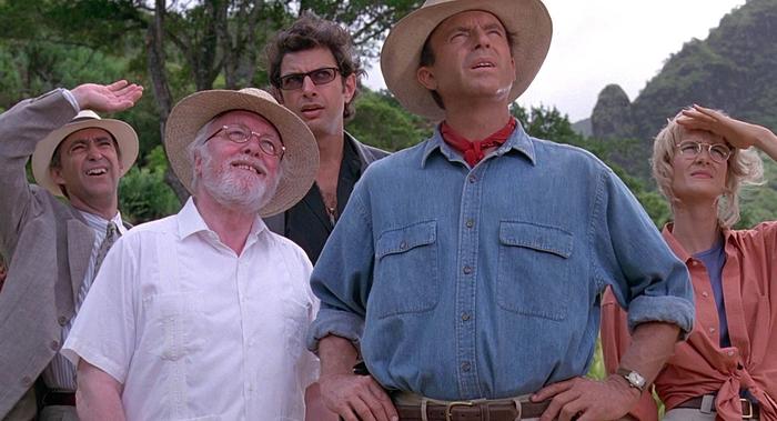The cast of the original Jurassic Park looking beyond in a forest.