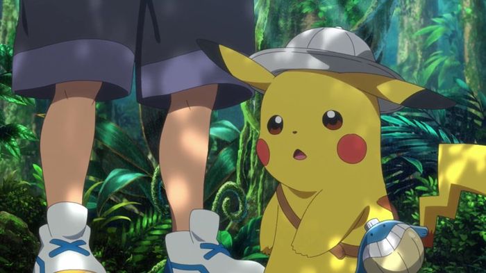 Pikachu wearing an explorer hat and looking shocked, with Ash's legs and the jungle behind it.