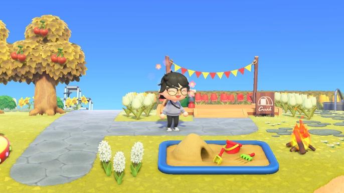A player using a joyful reaction by some flowers and a sandpit on their island in Animal Crossing New Horizons.