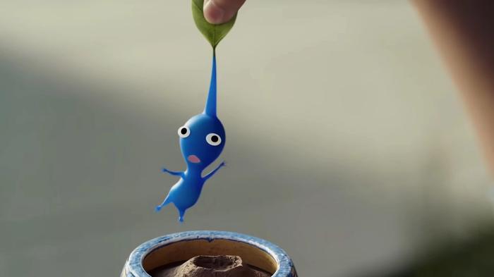 A Pikmin being lifted up by a giant human hand.