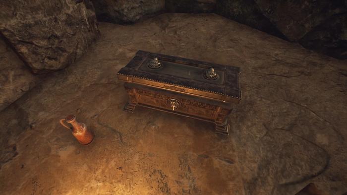 The Forgotten City. A chest with a bottle of wine next to it, hidden on a ledge in a cave. The wooden chest is in the middle and the orange bottle of wine is lower on the left.