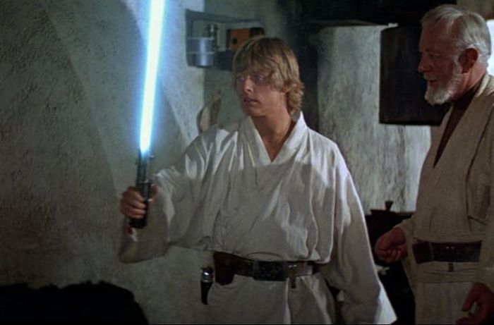 Luke holding Annakin's light saber. Obi-Wan is close by.
