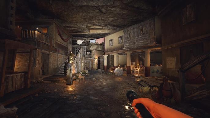 The Forgotten City, The Slums. The image shows the slums being lit by a torch beind held by the player. Livia is standing on the right with her back to the player. The slums are dimly lit with some cloth hanging from the ceiling at the back.