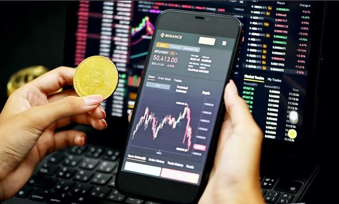 Person holding Bitcoin next to phone on Binance app.