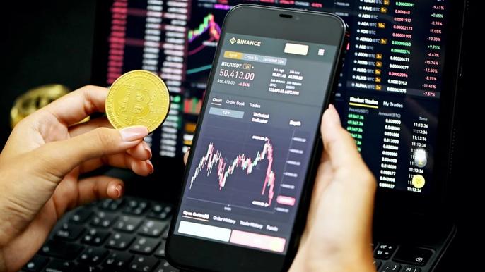 Person holding Bitcoin next to phone on Binance app.