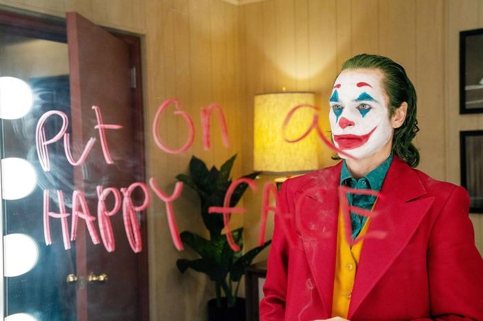 Joker looks at a mirror with "put on a happy face" written on it.