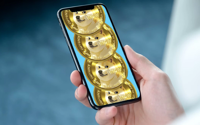 Image of four Dogecoin coins on a phone in a hand.