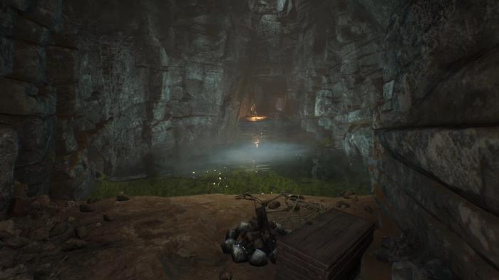 The Forgotten City. The tunnels under diana's shrine, first body of water with green algae in it. There is a fireplace, a chest and a skeleton to the right.  The cave is dim and there is an opening on the other side of the body of water. 