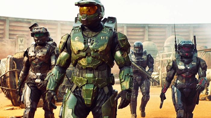 Four Spartans, including Master Chief, are walking in a desert-like environment.