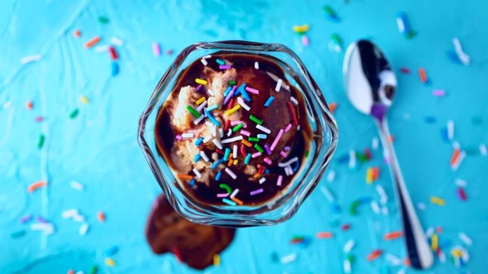 Image of Sundae on a blue background with sprinkles and a spoon.