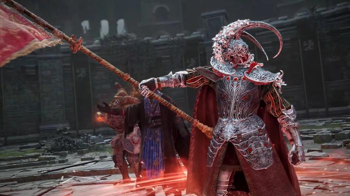 A man in red armour is pointing into the Colosseum in Elden Ring.