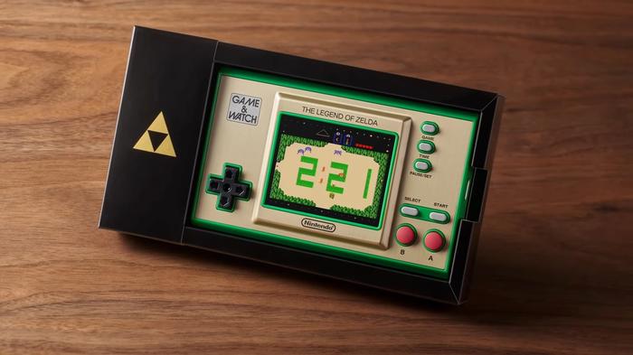 The Game & Watch: the Legend of Zelda handheld sits in its black dock, on a darkwood surface