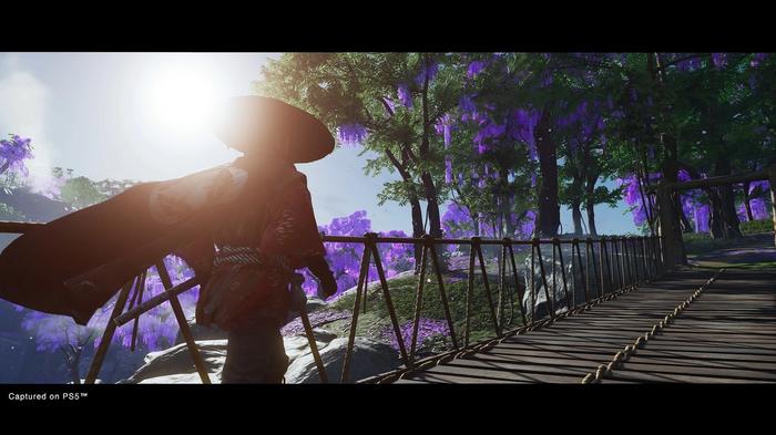 Screenshot from Ghost of Tsushima on PS5 Jin crossing a bridge with a series of purple-hued trees in the distance.
