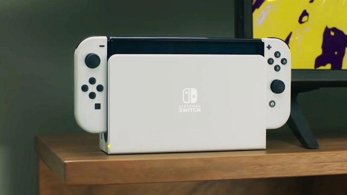 The white Nintendo Switch OLED stands on a wooden table.