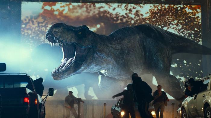 A dinosaur roars in front of a big screen.