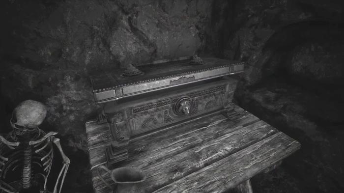 The Forgotten City. The treasure chest in the room behind the golden statue. The chest is on a wooden table and there is a skeleton to the left of the table on the floor. 