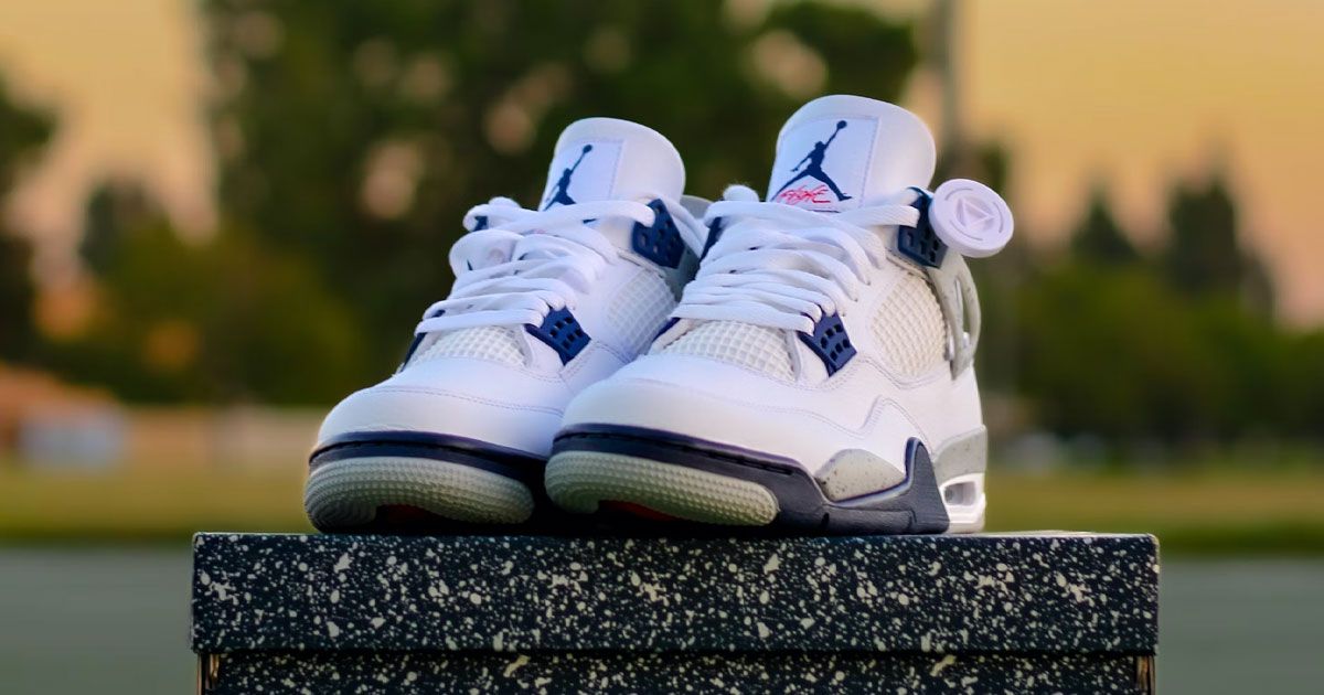 A pair of white Jordan 4s featuring blue trim and details sat on top of a black speckled box.