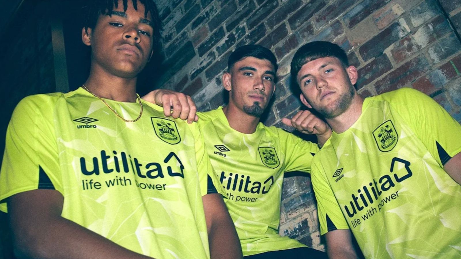 Huddersfield Town Umbro Away Kit product image of three people wearing highlighter yellow Umbro kits featuring black branding and sponsorship.