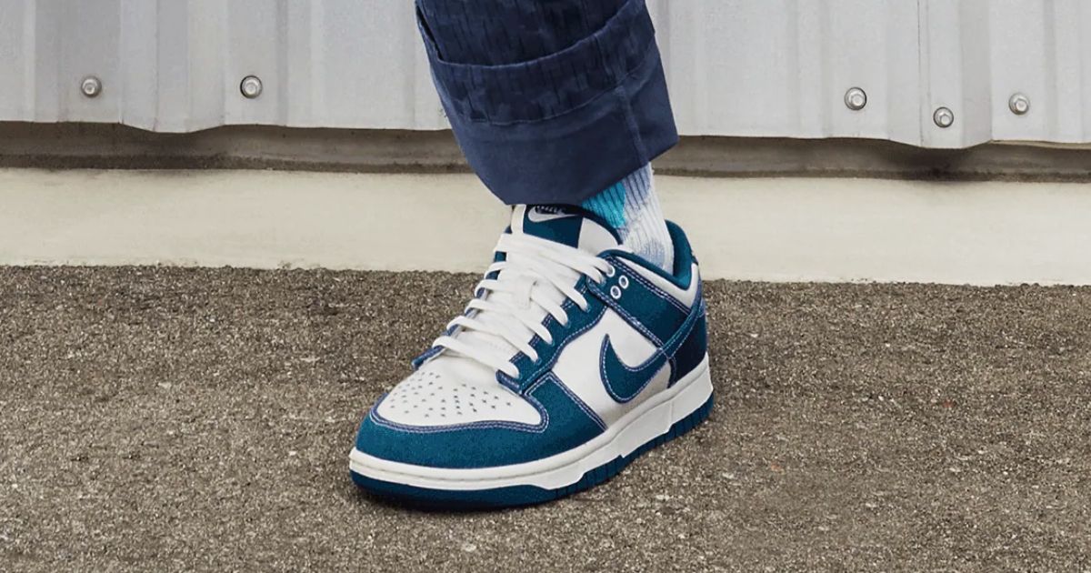 Someone in blue trousers wearing white leather and blue fabric Nike Dunk Lows.