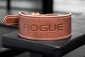 Image of a brown leather weightlifting belt featuring Rogue branding sat on top of a black weight bench.