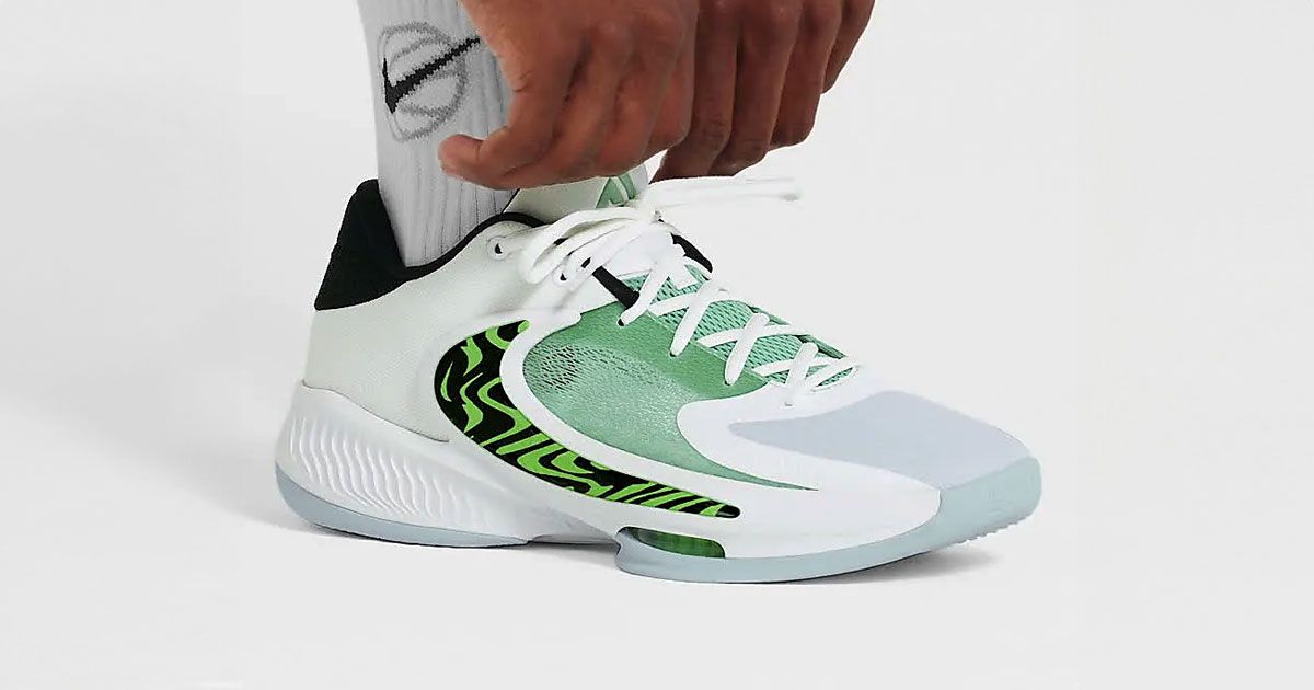 Someone in white socks adjusting a white and icy blue Nike Zoom Freak 4 with black and green details.