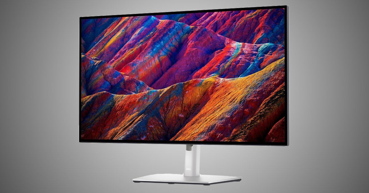 Dell UltraSharp U2723QE product image of a silver and black near-frameless monitor with purple, blue, and orange hilltops on the display.