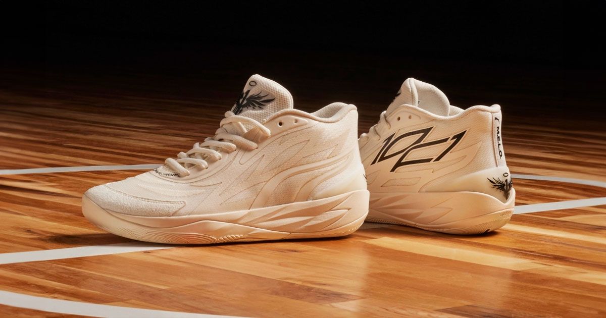 A pair of white PUM MB.02 basketball shoes with black trim and branding sat on a hardwood basketball court.