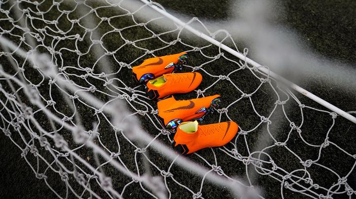 A collection of four bright orange Nike football boots in a football net.