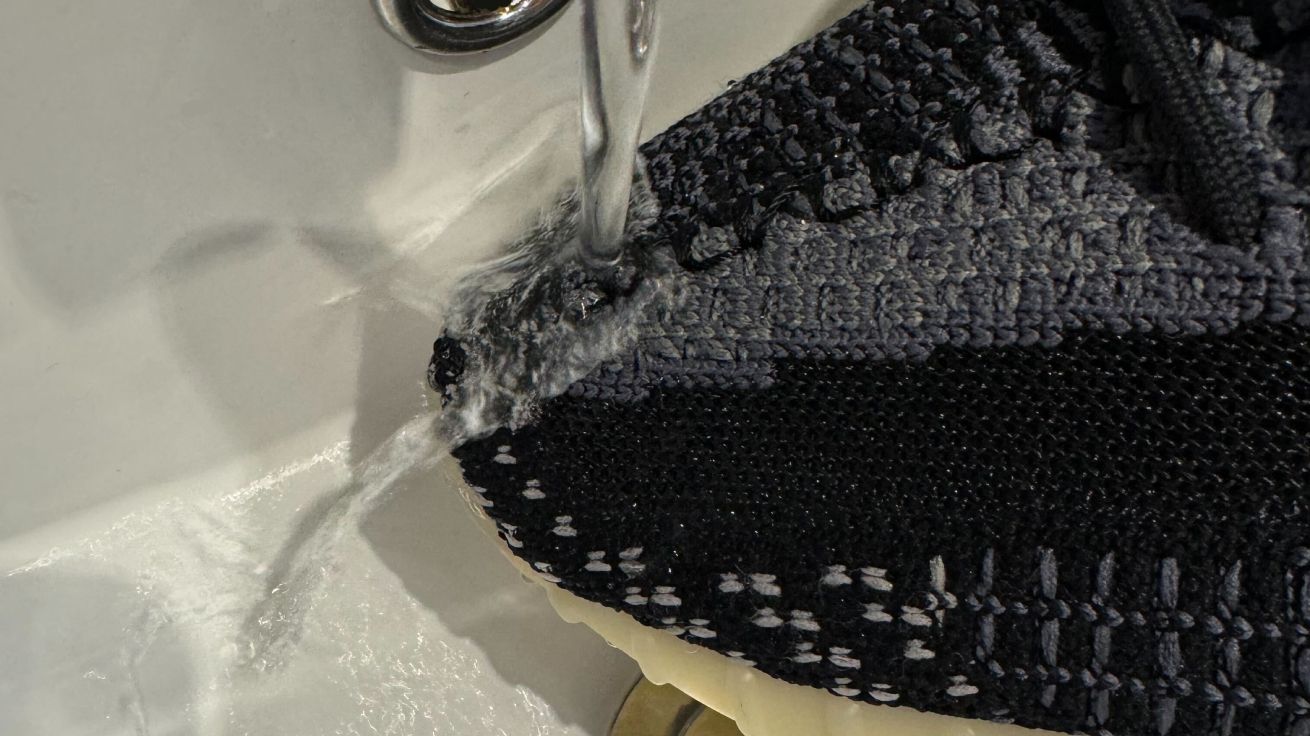 A close-up of a black knitted Yeezy with running water flying straight off it.