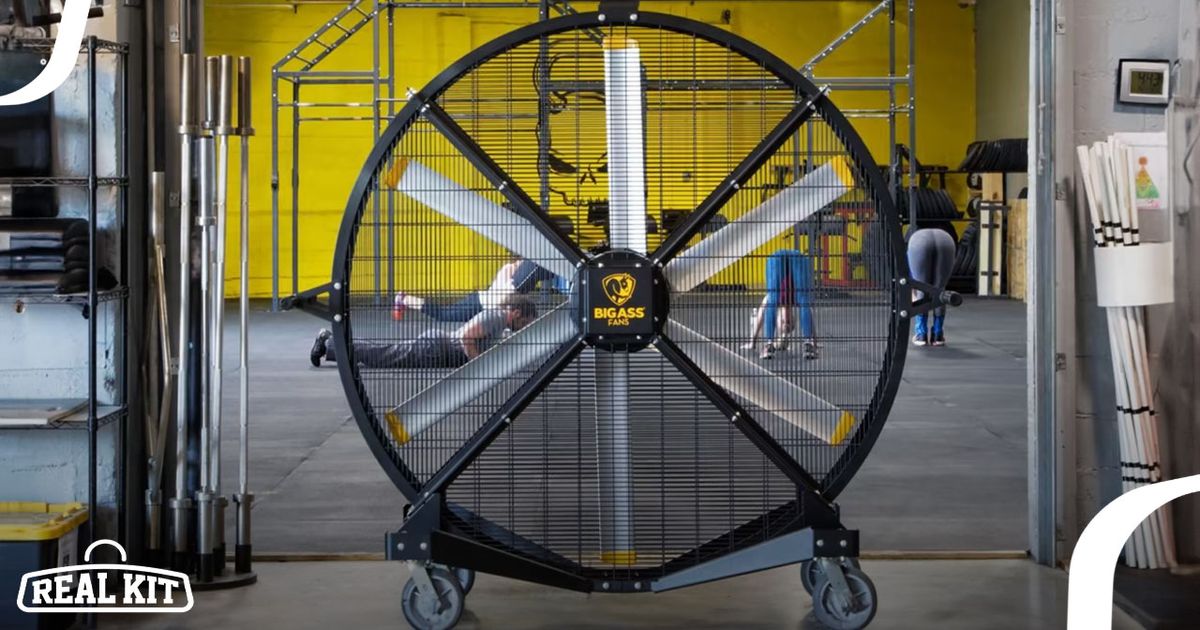 A large black floor fan with yellow branding placed in a gym with a yellow back wall.