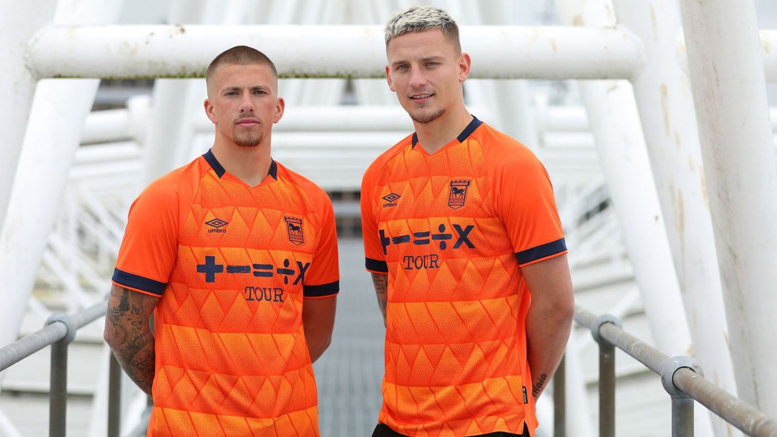 Ipswich Town Umbro Away Kit product image of two players wearing bright orange shirts with black collars and sleeves along with Ed Sheeran's album logos as the sponsor.