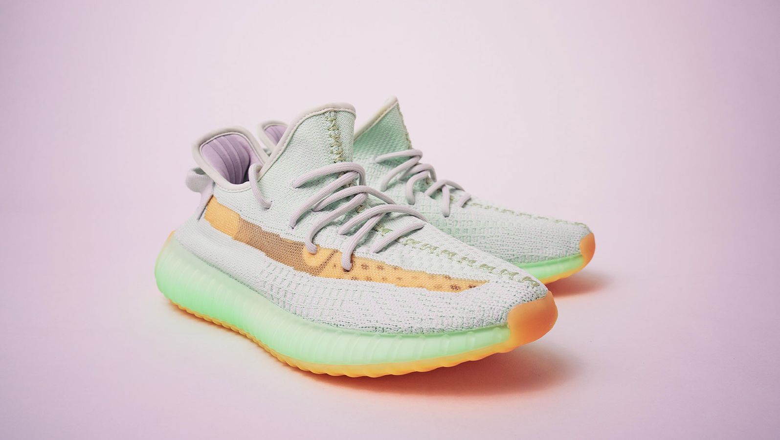 adidas Yeezy product image of a mint green and orange pair of sneakers with a pink backdrop.