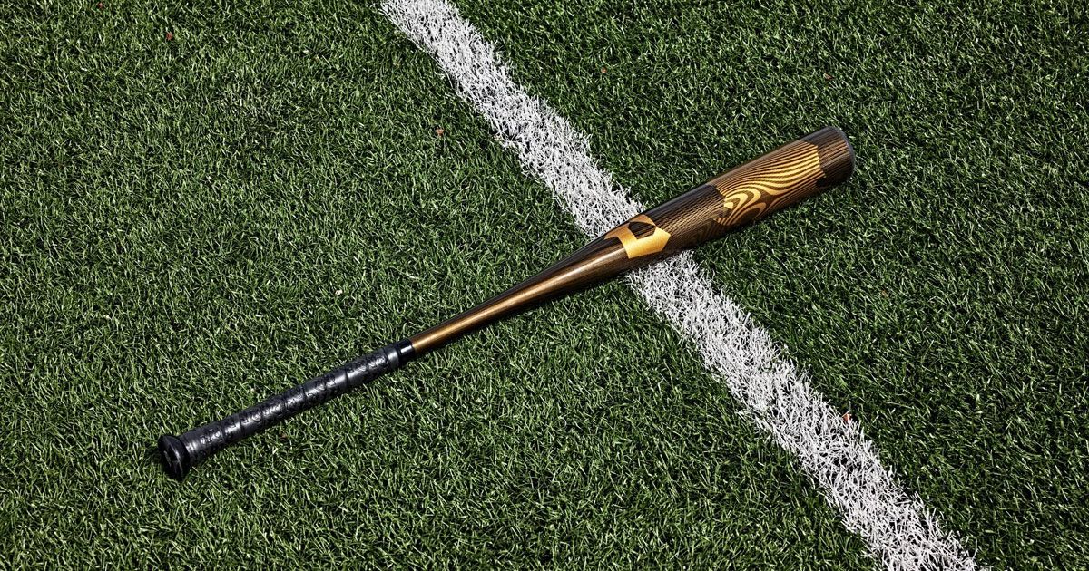 A black, brown, and gold baseball bat laying on a green artificial surface.
