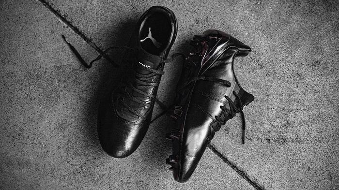 A pair of black PUMA football boots laying on grey ground..