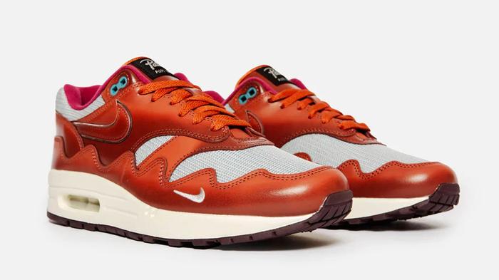 Patta x Nike Air Max 1 product image of a burnt orange and grey pair of sneakers on feet.