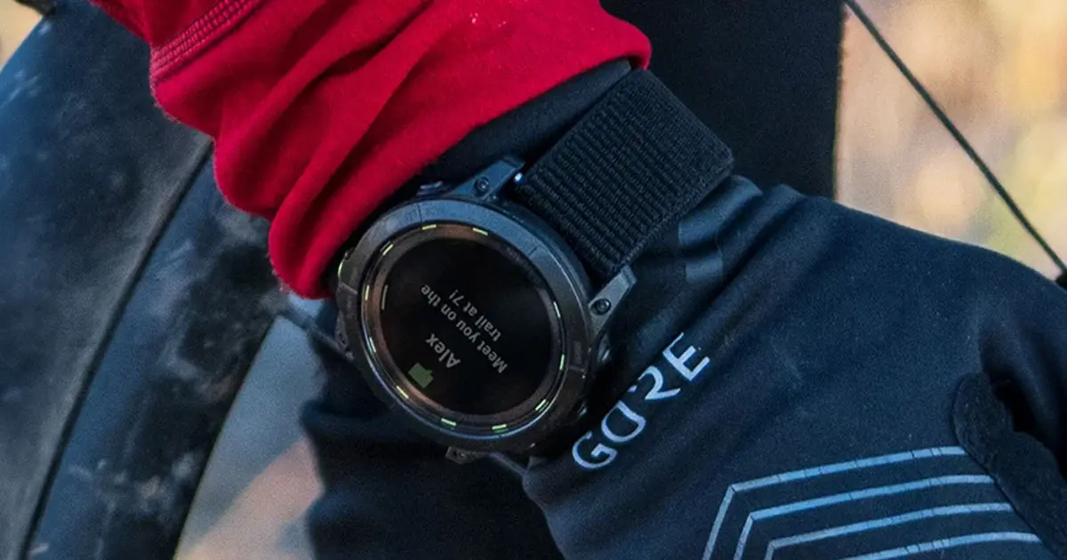 Close-up of someone in a red jacket and black GORE-TEX gloves wearing a black smartwatch.