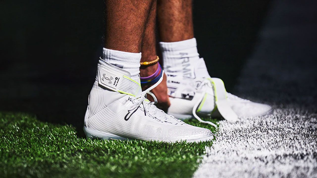 Someone adjusting a pair of white high-top football cleats on their feet.