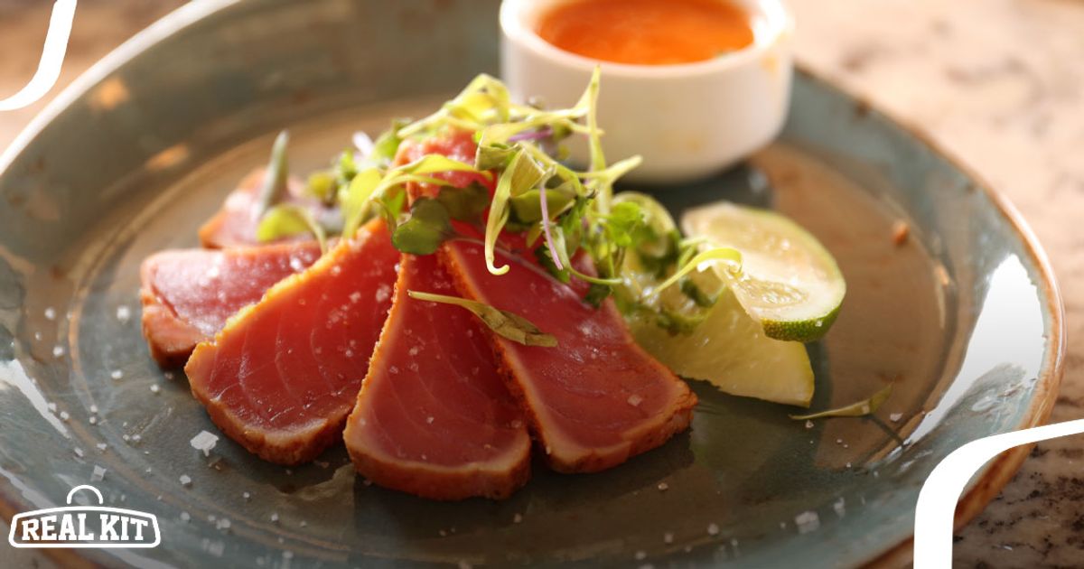 Image of three pieces of seared tuna with garnish and an orange sauce.