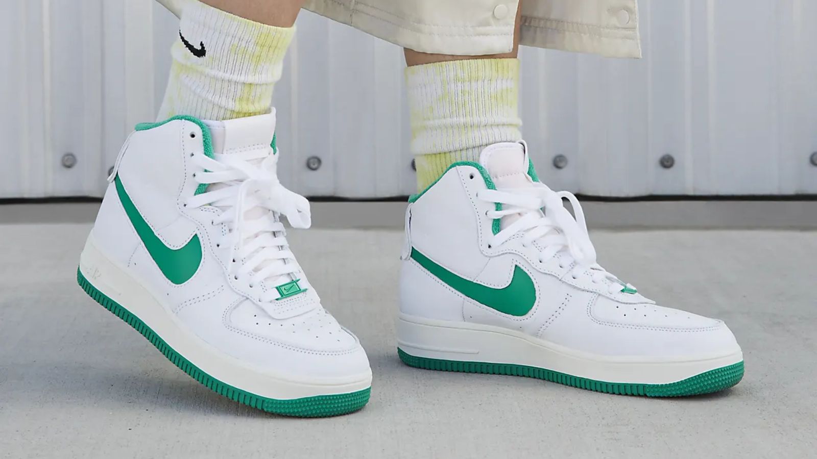 Someone in washed white and yellow Nike socks wearing white and green Air Force 1 high-tops.