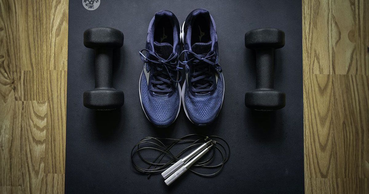 A pair of blue and white trainers sat on a yoga mat next to a set of black dumbbells and a black skipping rope.