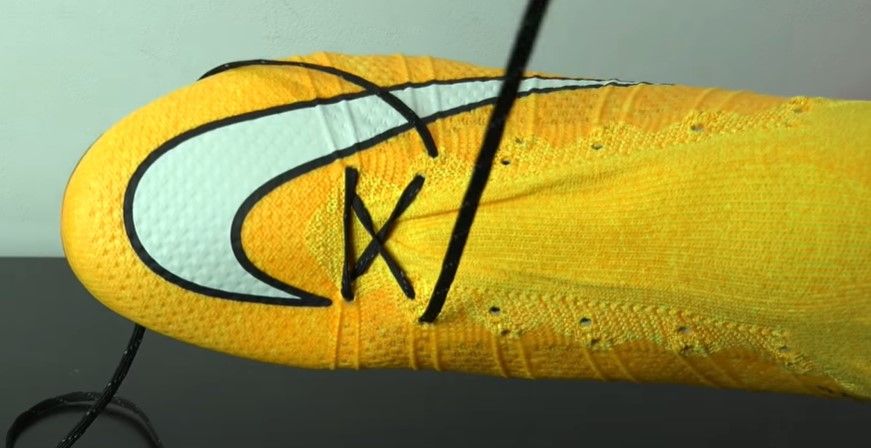 A yellow and orange Nike football boot featuring a white Swoosh and black laces.